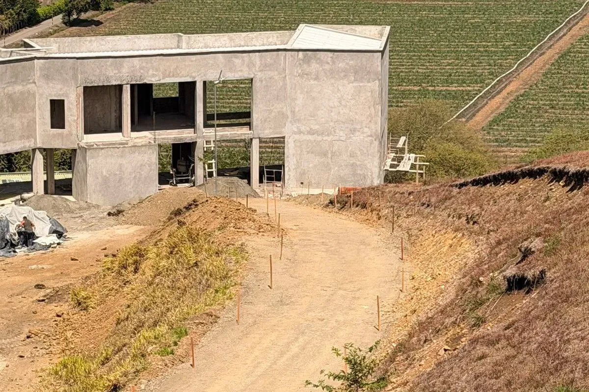 Two-storey house at the structure stage on a hillside platform, with an access road in front