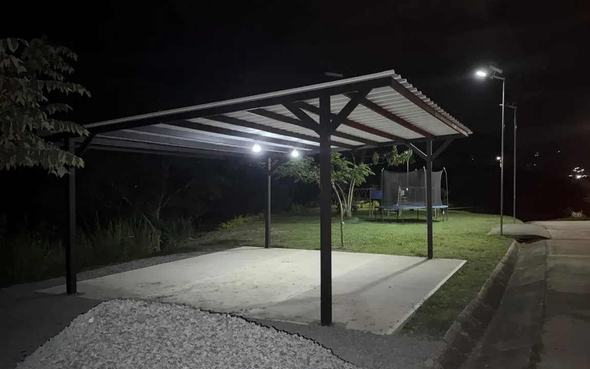 Covered shelter with a concrete floor, lit at night, next to an internal road with street lighting
