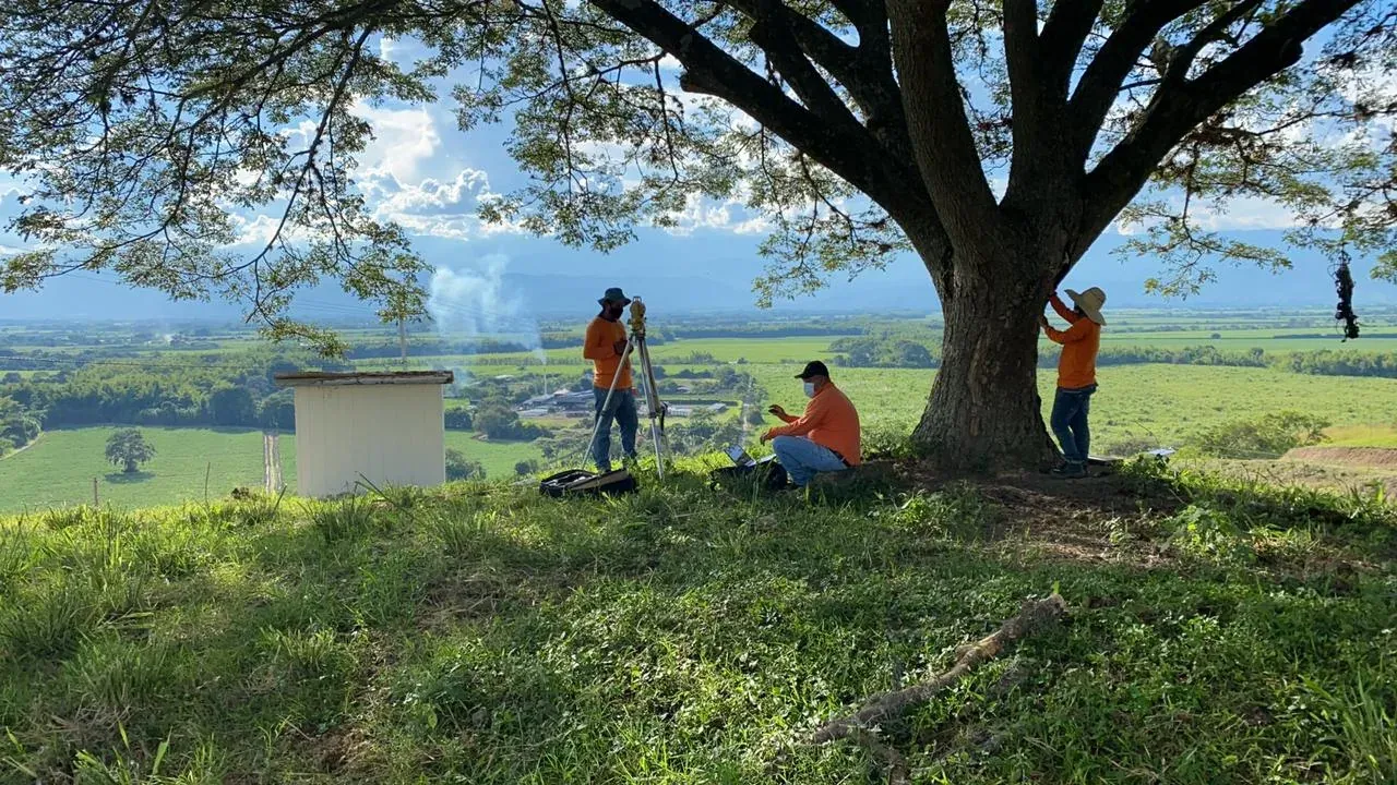 Survey crew working with a total station under a large tree, with the valley in the background